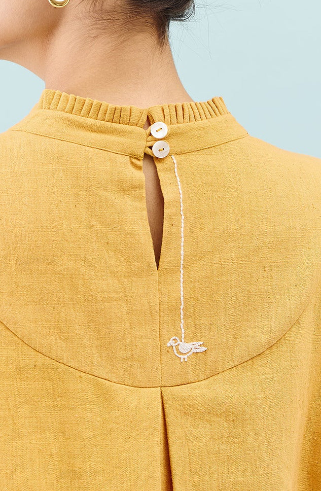 Woman wearing a mustard yellow blouse with a light blue background