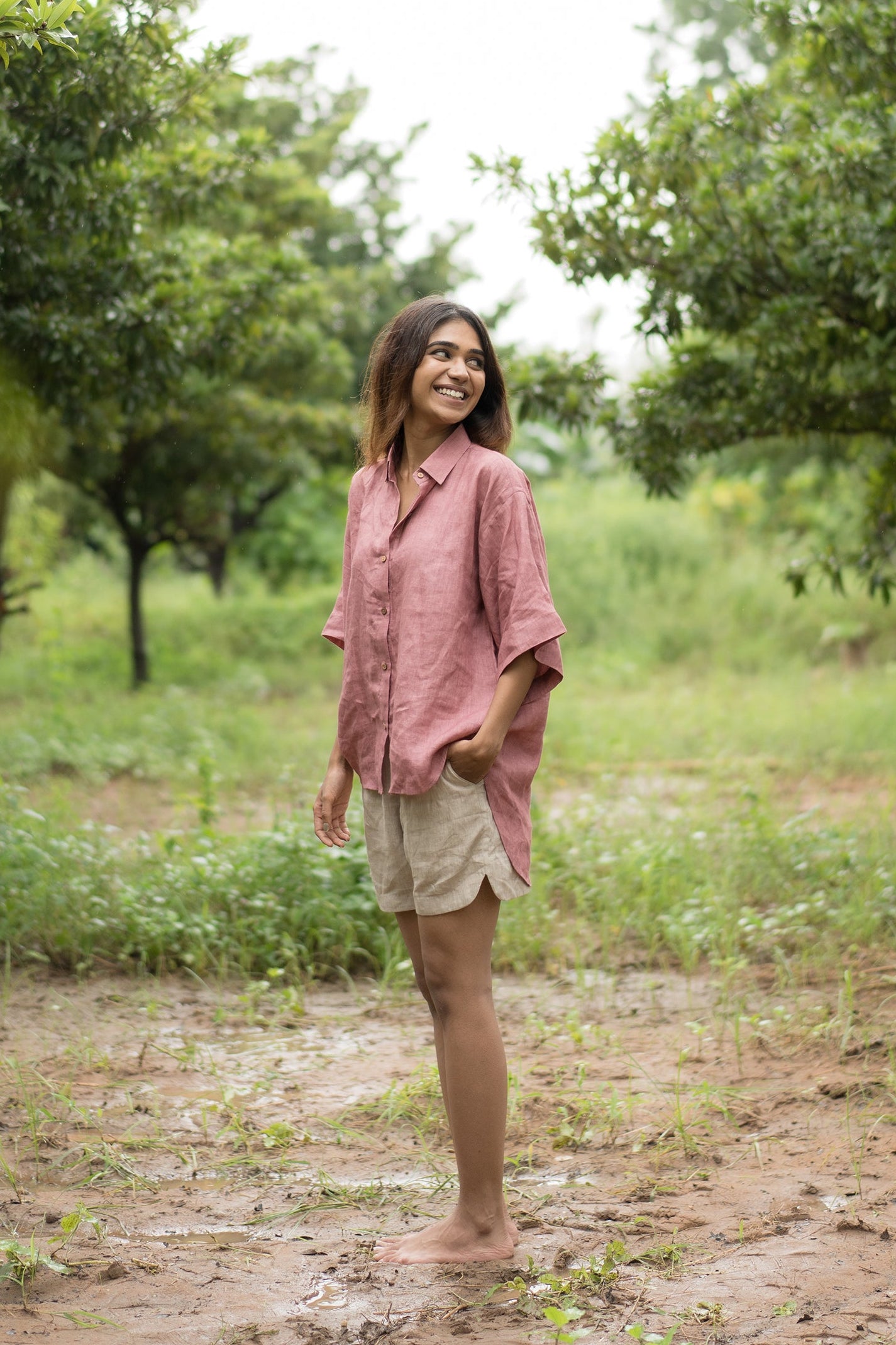 Woman standing in a field with trees in the background wearing a linen shirt.